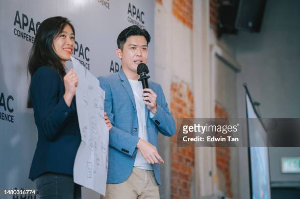 asian chinese woman sharing her concept and idea on stage with emcee host in apac conference event - compere stock pictures, royalty-free photos & images