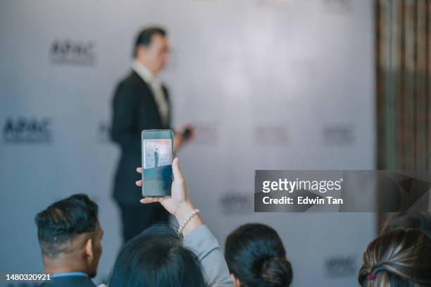 asian chinese female seminar participant raise arm, taking photo of presenter speaker with smart phone in business conference - kick off call stock pictures, royalty-free photos & images