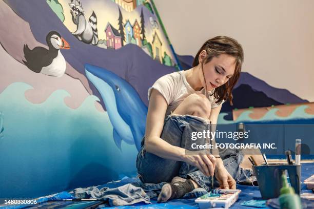 young female artist painting mural in the attic - painting mural stock pictures, royalty-free photos & images