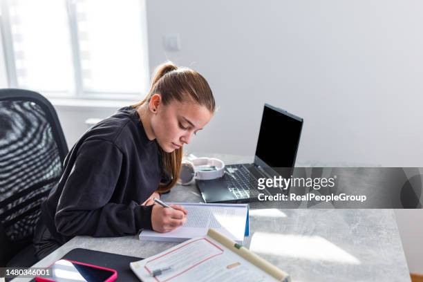 teenage girl taking notes on notepad while using laptop - pen paper stock pictures, royalty-free photos & images
