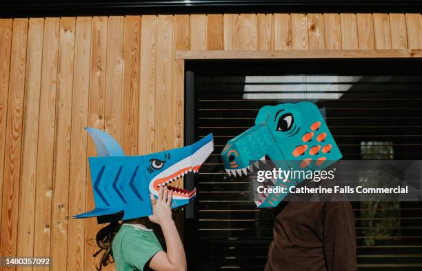 siblings face each-other, wearing fun, colourful homemade fearsome animal masks. - depictions stockfoto's en -beelden