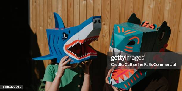 siblings wear fun, colourful homemade fearsome animal masks. - depictions stockfoto's en -beelden