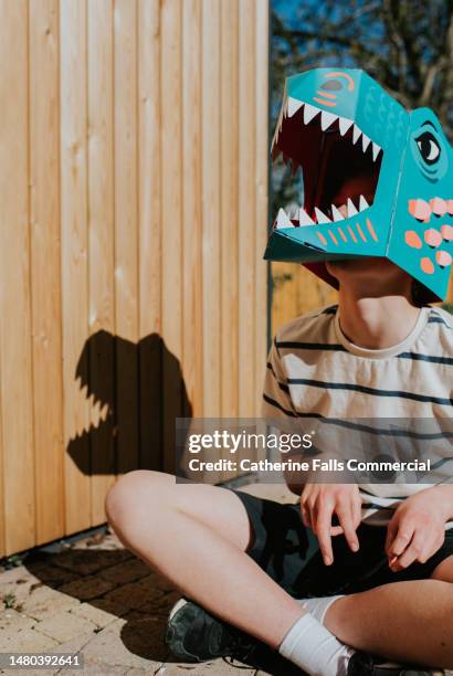 an older boy wears a dinosaur mask - toy animal stock pictures, royalty-free photos & images