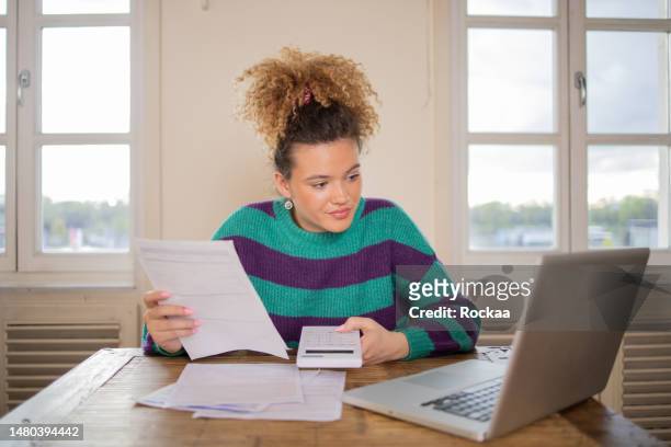 young woman using calculator while going through bills and home finances - student loan stockfoto's en -beelden