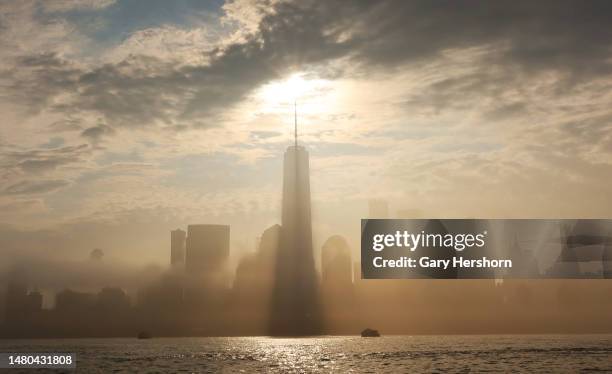 The sun rises behind the skyline of lower Manhattan and One World Trade Center as a morning fog lifts in New York City on April 6 as seen from Jersey...