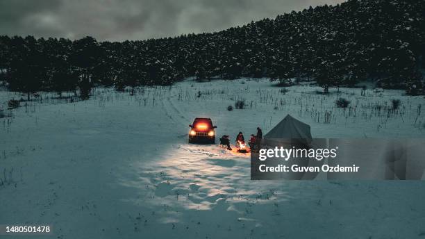 people spending winter holidays in forest, friends camping on shore of snow-covered winter lake at twilight, camping on snowy mountain, mountain travelers warming up by campfire, aerial view of winter camp - car warming up stock pictures, royalty-free photos & images