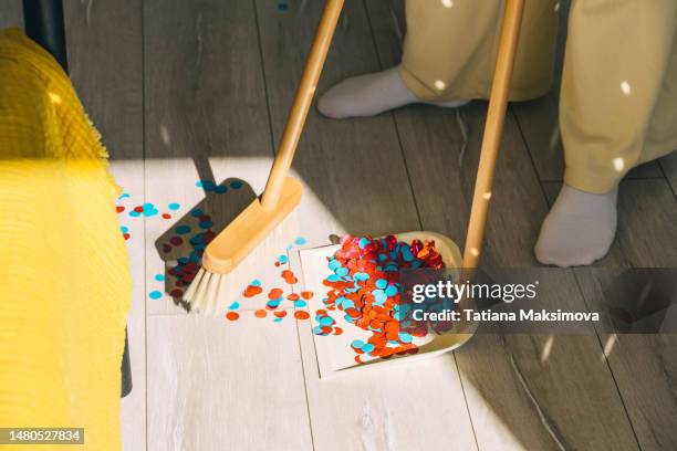 a beautiful young woman sweeps confetti from the floor with a wooden mop after a party. - messy house after party stock-fotos und bilder