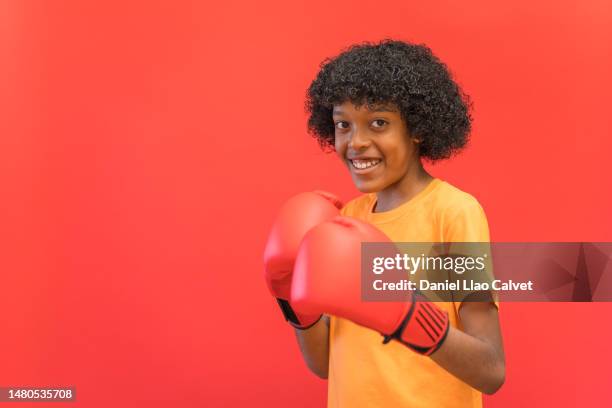 boy wearing boxing gloves standing against red background - fondo rojo stock pictures, royalty-free photos & images