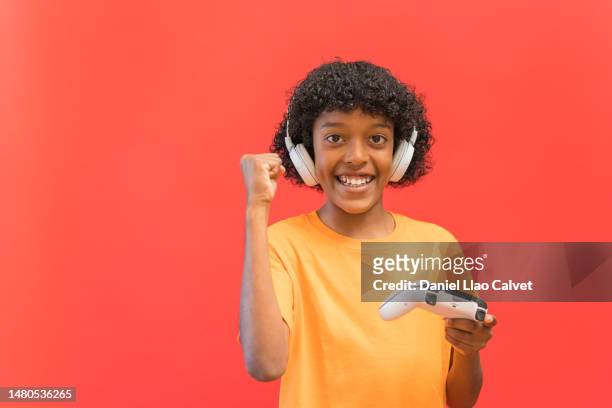a preteen boy plays a video game while raising his fist - fondo rojo stock pictures, royalty-free photos & images
