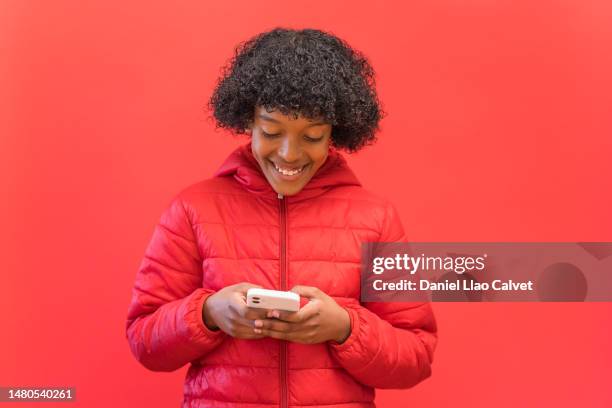 happy african american boy using a smartphone on red background. - fondo rojo stock pictures, royalty-free photos & images