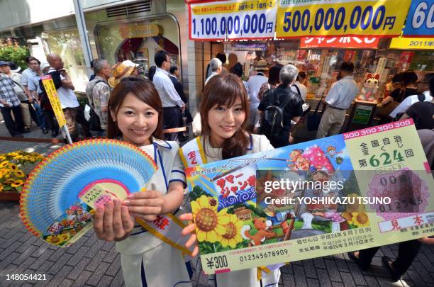 Campaign staff Mayuka Nakatani and Manami Murakami display sample lottery tickets as people queue to purchase tickets for the 500 million yen summer...