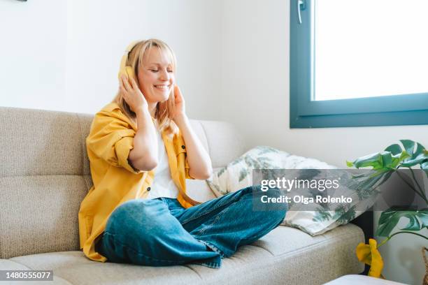 good vibe and good music for mental health. calm blond woman holding yellow headphones on her head, relax with good music on a sofa - aura foto e immagini stock