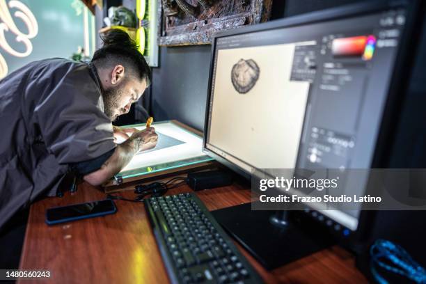 jeune homme dessinant sur papier dans un studio de tatouage - photoshop photos et images de collection