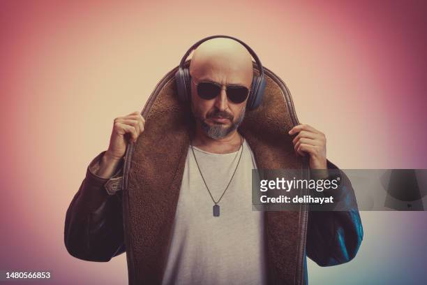exzentrischer und charismatischer mann mit glatze in langem pelzmantel und weißem tanktop mit kopfhörern und sonnenbrille - rap stock-fotos und bilder