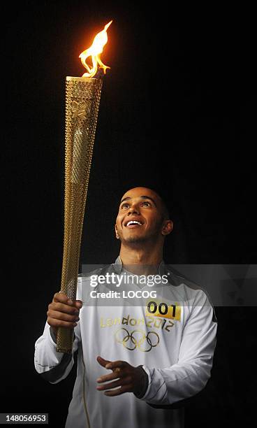 In this handout image provided by LOCOG, Formula One driver and Torchbearer 001 Lewis Hamilton holds the Olympic Flame before his Torch Relay leg...