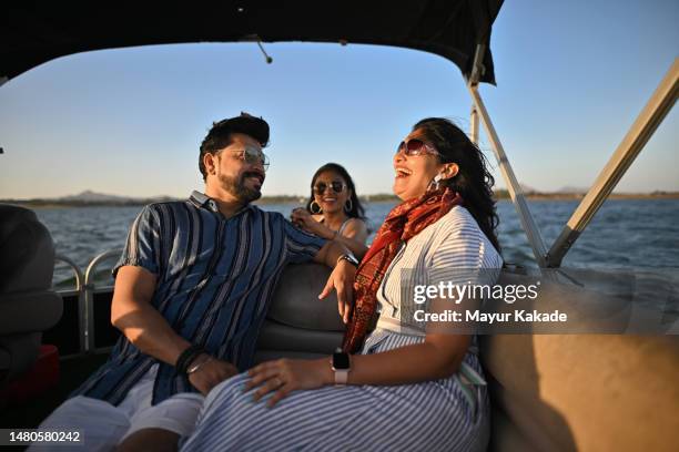 a dynamic mid adult couple with their teenage daughter enjoying a boat ride on a lake. - indian family vacation stock pictures, royalty-free photos & images
