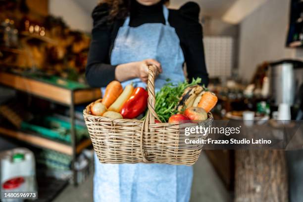 verkäuferin, die einen korb mit obst und gemüse in einem kleinen lokalen laden hält - markthalle stock-fotos und bilder