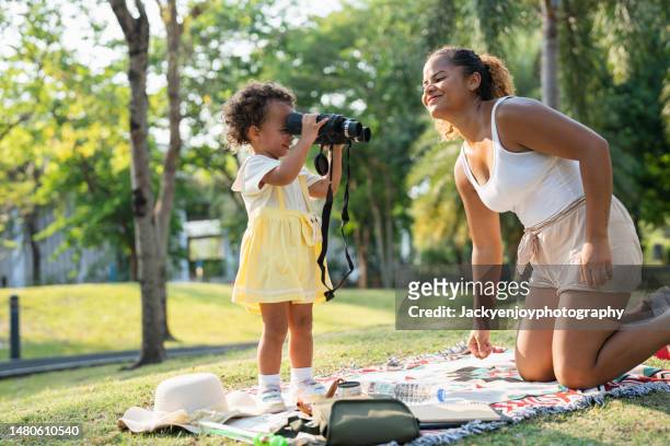 young mother and lovely little daughter spending time together outdoors, playing with binoculars and smiling joyfully in park on a lovely sunny day against beautiful blue sky - asian child with binoculars stockfoto's en -beelden