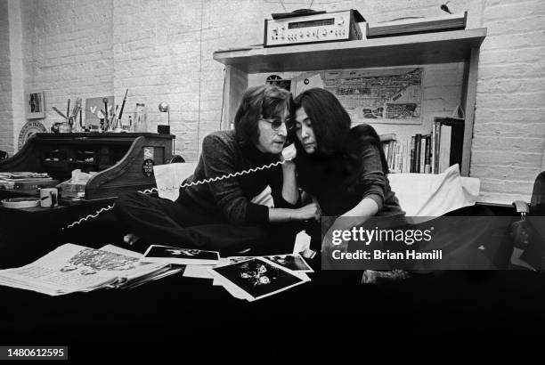 View of married couple, British musician John Lennon and Japanese-born artist & musician Yoko Ono, as they share a telephone receiver while seated on...