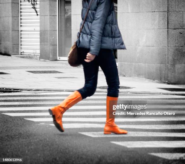 young woman crossing the street with orange boots. - oranje laars stockfoto's en -beelden