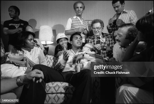 Surrounded by others. American boxer Muhammad Ali , his infant daughter Laila in one arm, speaks to members of the press in his hotel suite, New...