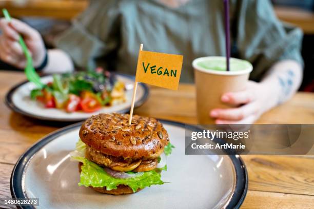 frau isst gemüsesalat und burger mit dem wort "vegan" auf einer kleinen fahne in einem vegetarischen restaurant oder food court - vegan stock-fotos und bilder