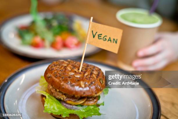 woman eating veggie burger with "vegan" word on small flag  on a plate in a veggie restaurant or food court - burger with flag stock pictures, royalty-free photos & images