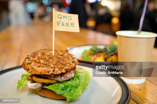 vegan burger with "gmo free" words on small flag  on a plate in a veggie restaurant or food court - burger with flag stock pictures, royalty-free photos & images