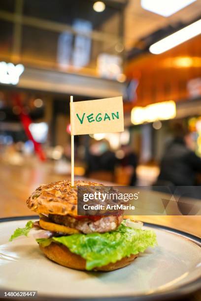 vegan burger with "vegan" word on small flag  on a plate in a veggie restaurant or food court - burger with flag stock pictures, royalty-free photos & images
