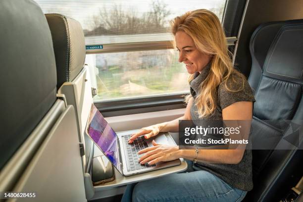 woman on the train at the laptop - woman blond looking left window stockfoto's en -beelden