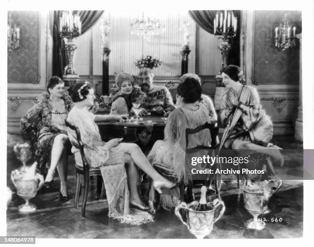 Five women dressed as flappers sit around a table laughing in a scene from the film 'The Wedding March', 1928.