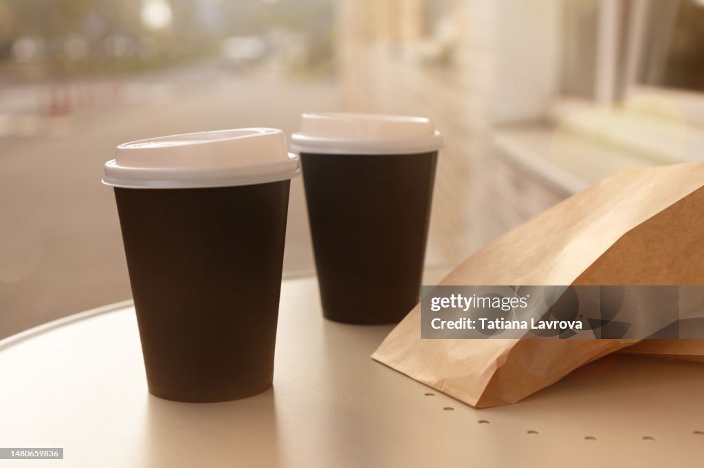 Two paper coffee cups on table with copy space. Warm spring (summer) street on the background. Food and drinks to go. Lifestyle photography without people