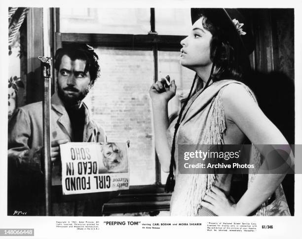 Man standing with paper as Shirley Anne Field smokes a cigarette in a scene from the film 'Peeping Tom', 1960.