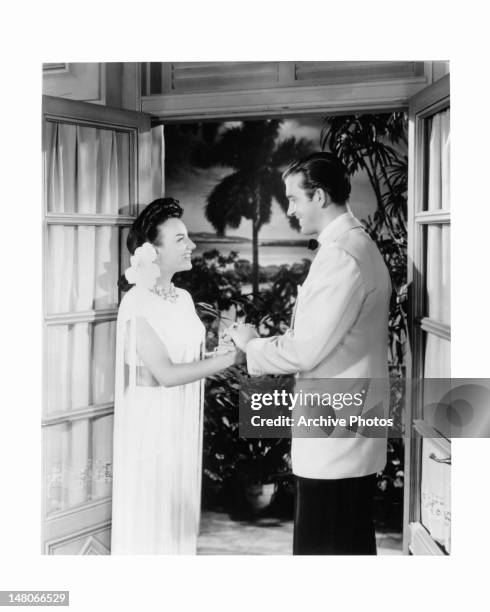 Carmen Miranda stands holding a man's hand in a scene from the film 'Week-End In Havana', 1941.