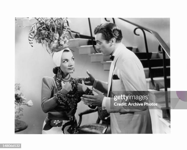 Carmen Miranda dressed ornately from head to toe as she stands with a man talking to her in a scene from the film 'Week-End In Havana', 1941.