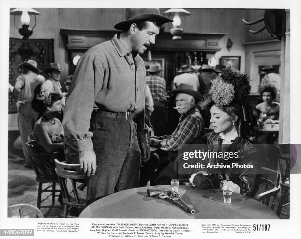 John Payne looking at gun on Arleen Whelan's table in a scene from the film 'Passage West', 1951.