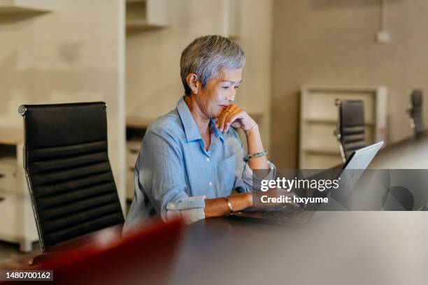 senior asian businesswoman working night shift in office - werkende bejaarden stockfoto's en -beelden