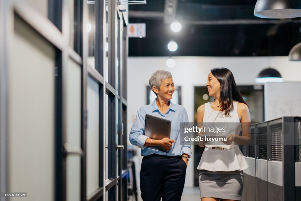Two asian businesswomen walking at office corridor and having discussion