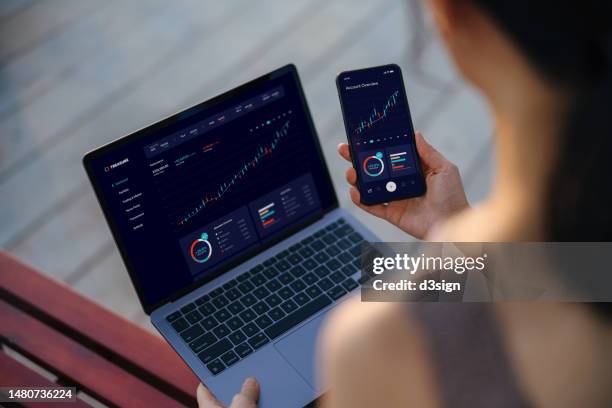 over the shoulder view of asian businesswoman managing finance and investment online, analyzing stock market trades and making financial plan with laptop and smartphone. online banking. banking, finance, investment and financial trading concept - financial accessory stock pictures, royalty-free photos & images