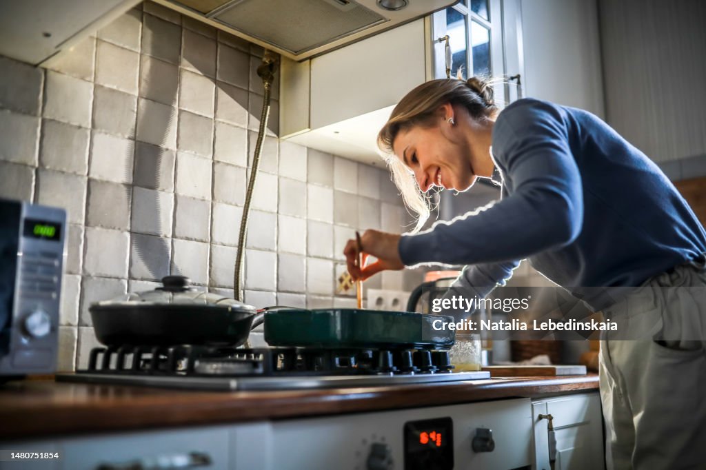 Mid adult woman with an amputated right arm cooking in kitchen at cozy home. Low angle view.