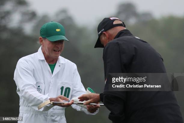 Sandy Lyle of Scotland's caddie Ken Martin hands Lyle a replica gold putter from his 1988 Masters win as he prepares to putt on the 18th green during...