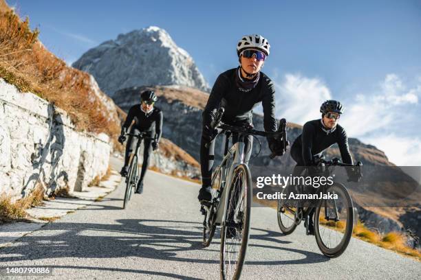 a trio of professional cyclists, one of them a woman, conquering the mountains together - racefiets stockfoto's en -beelden