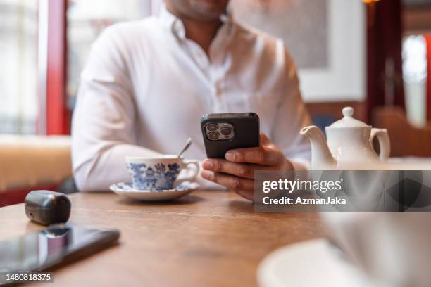 hand of a dark-skinned man holding an iphone over the table of a café - hands zoom in stock pictures, royalty-free photos & images