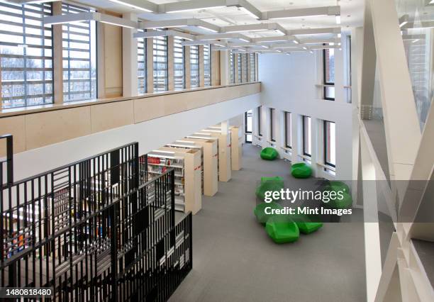 a healthcare college library with open spaces, green chairs and book stacks. a modern light and airy building - building atrium stock pictures, royalty-free photos & images