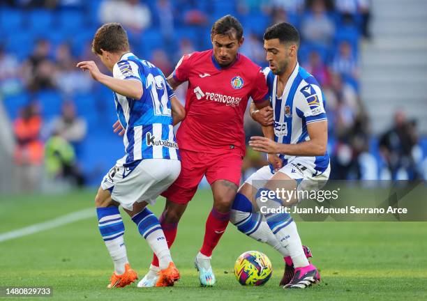 Damian Suarez of Getafe CF is challenged by Aihen Munoz and Mikel Merino of Real Sociedad during the LaLiga Santander match between Real Sociedad and...
