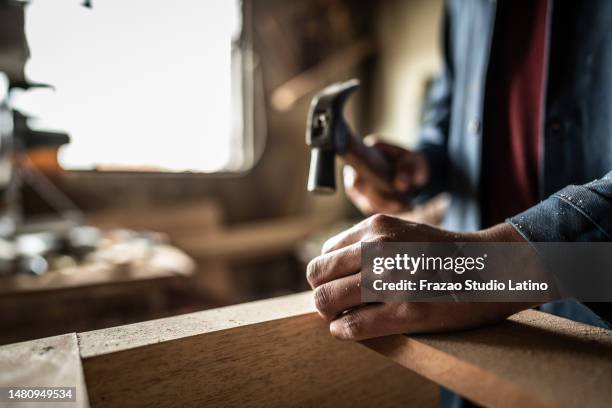 close-up of man hammering a nail on piece of wood - hamer handgereedschap stockfoto's en -beelden