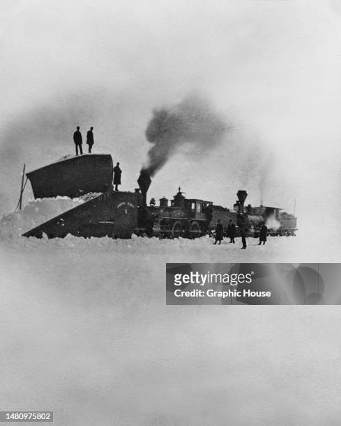 People standing on or beside a steam locomotive fitted with a snow plow as the region suffered what became known as the 'Hard Winter' (also known as...