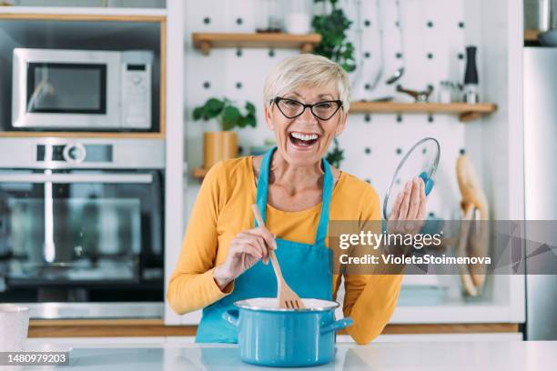 happy senior woman preparing lunch in modern kitchen. - white cooking pan stock pictures, royalty-free photos & images