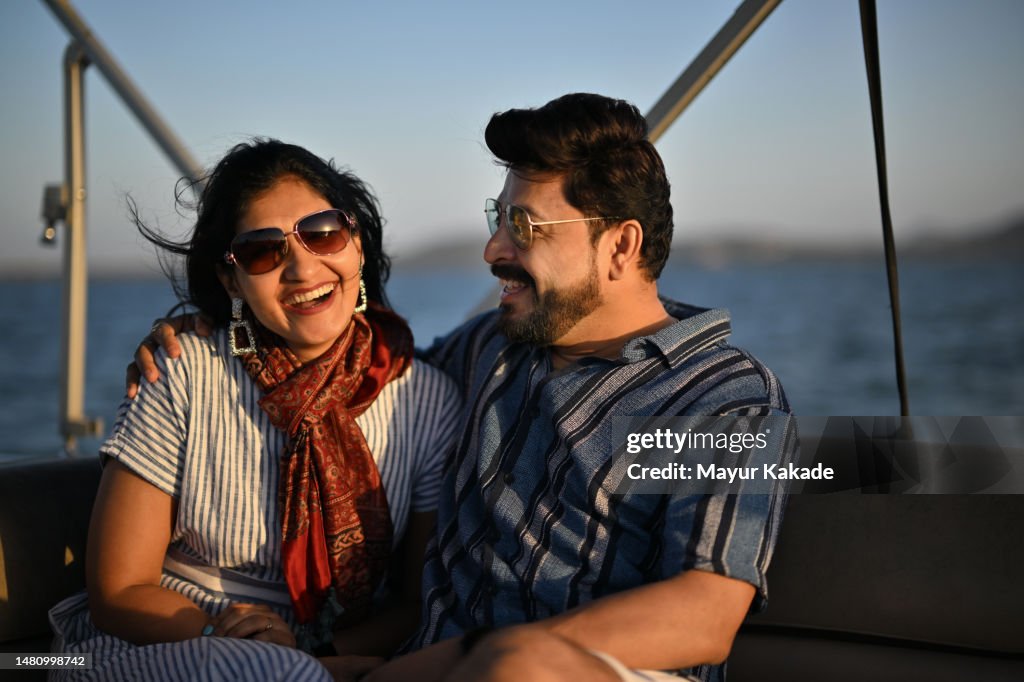 A mid- adult couple sharing laughter together on a boat ride enjoying sunset.