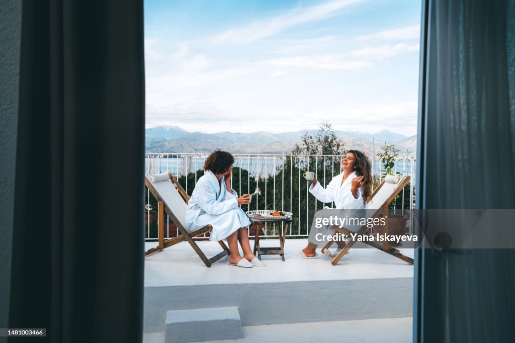 Two friends having a good time drinking tea with the scenic view on the balcony